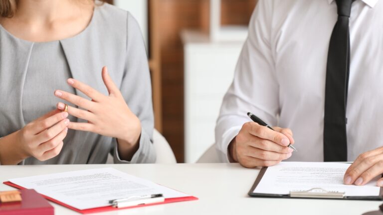 Woman takes off her ring while man signs divorce papers